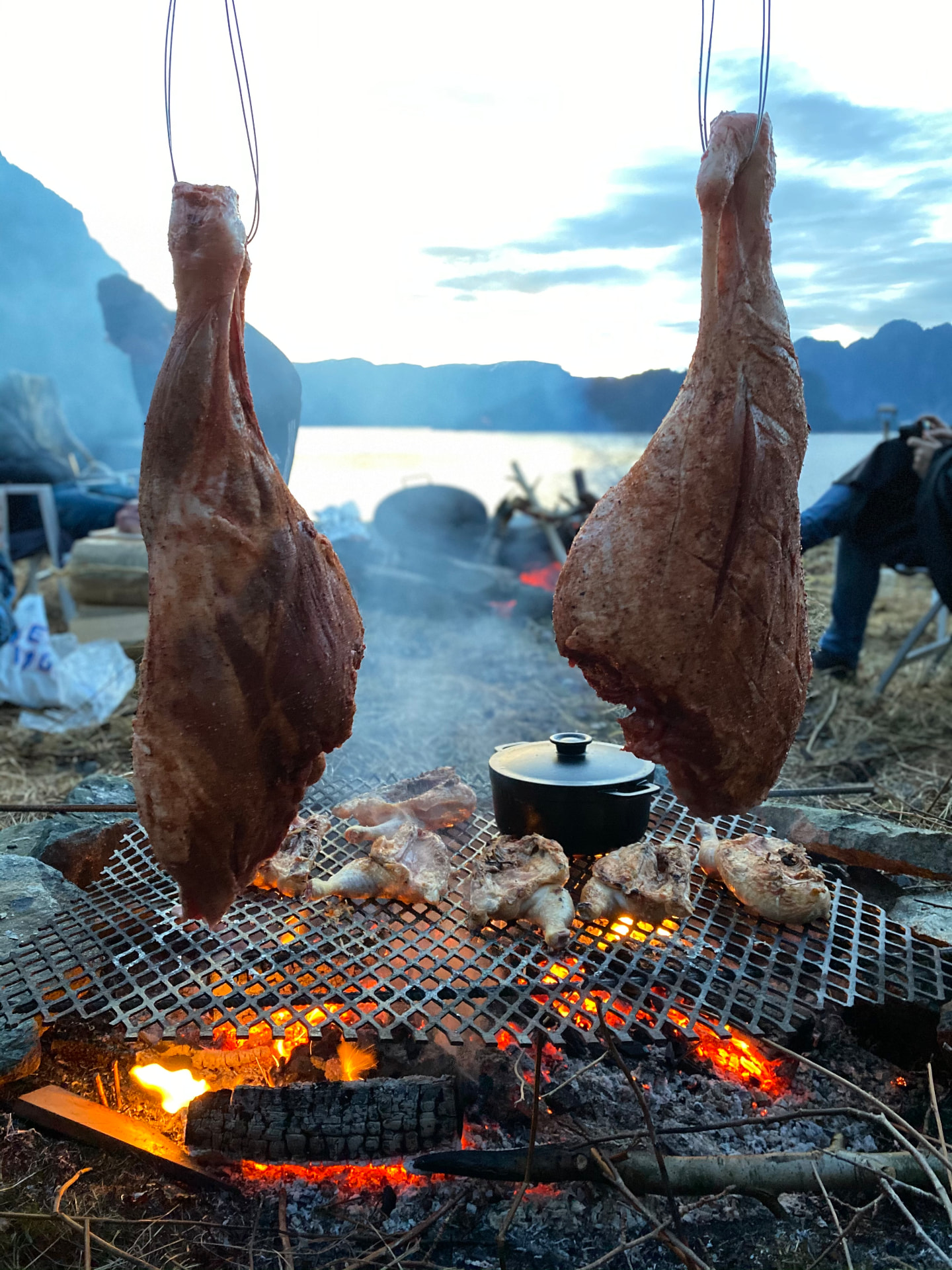 Kjøtt henger over glødende kullgrill ved vannet